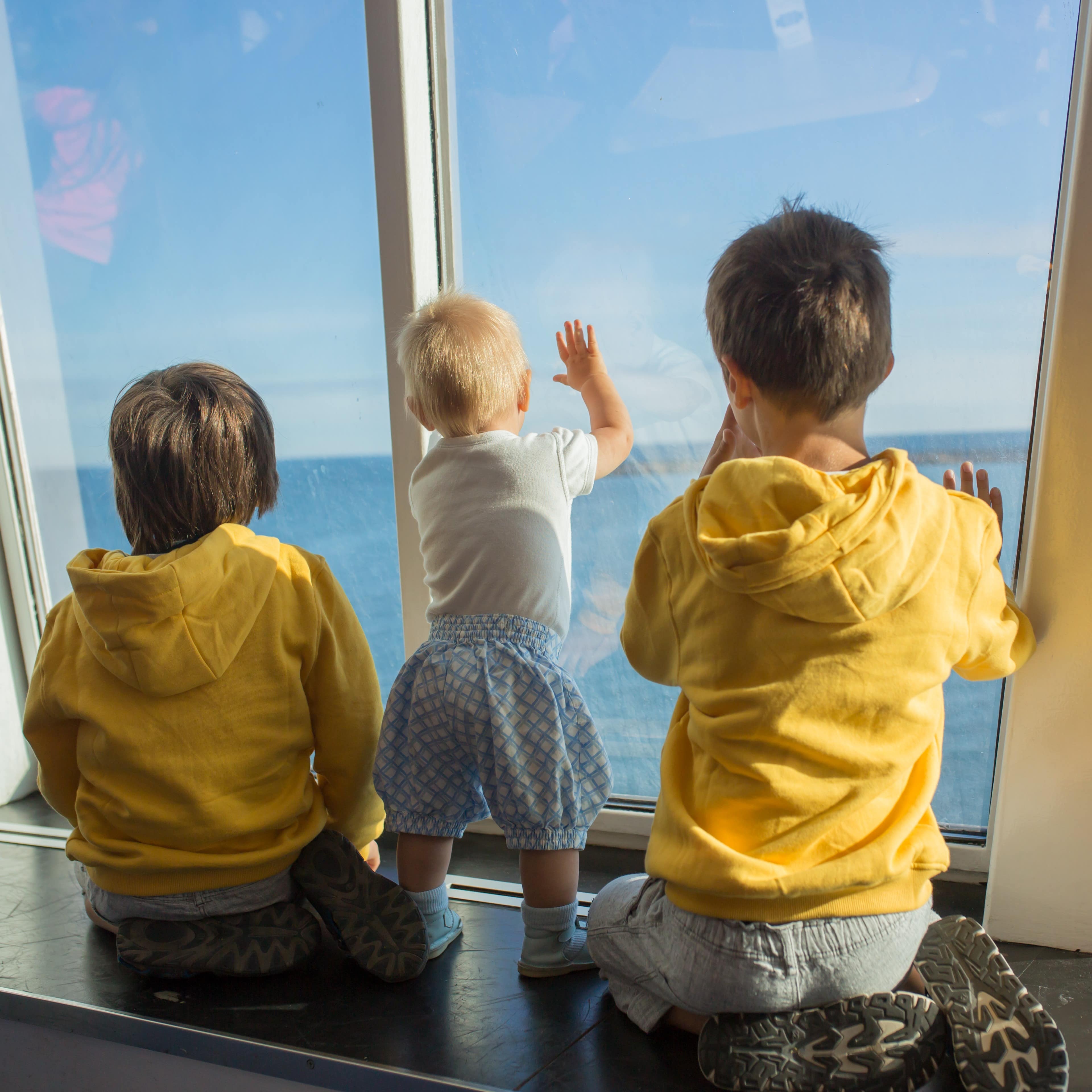 Two young children and toddler looking at the window while riding onboard a ferry